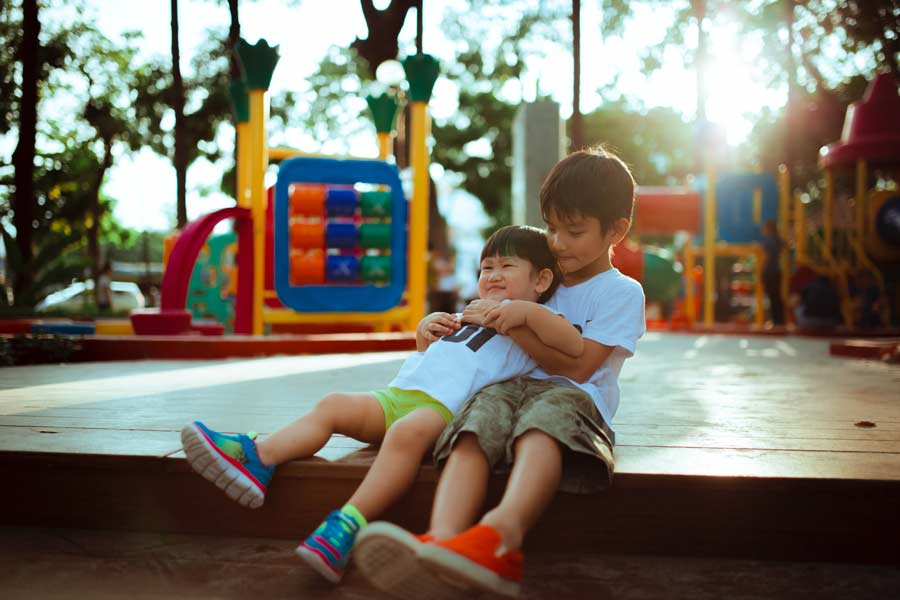 Older boy and younger boy playing on a playground with a variety of age-specific equipment