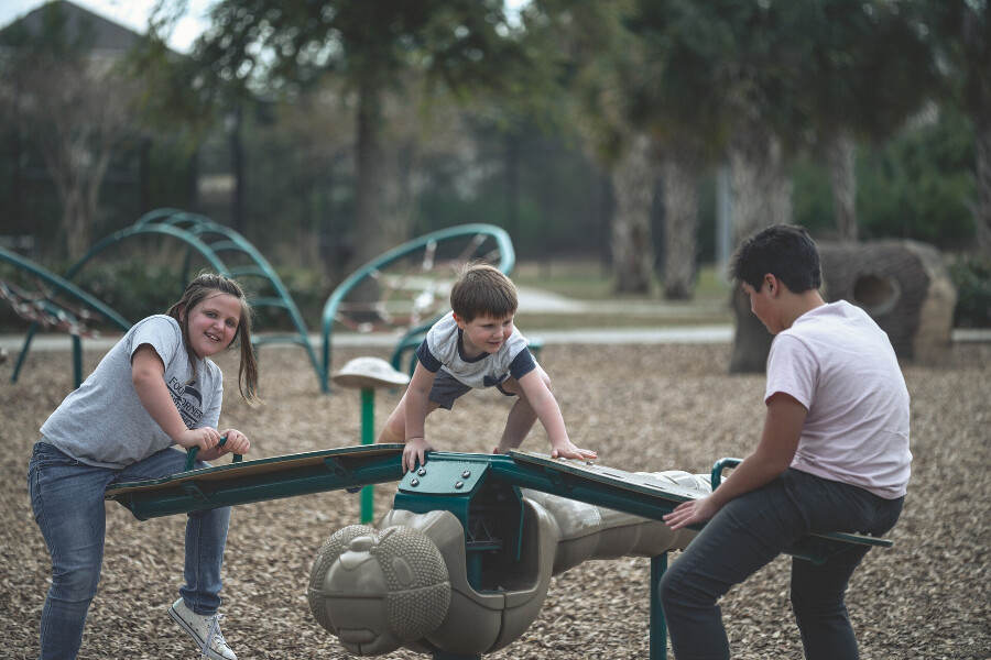 Three children playing on a seesaw in a park.