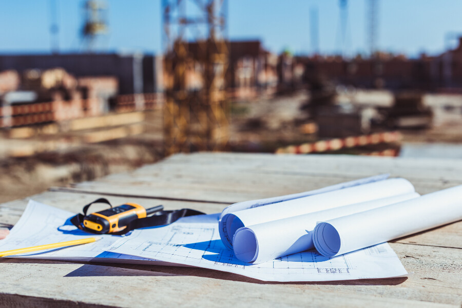 A close up of design-build plans with a construction site in the background - Construction Contractors Companies in Austin, TX