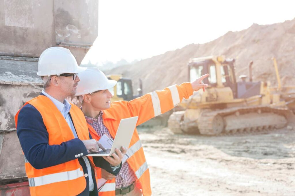 Supervisors with a laptop on a construction site wearing safety gear