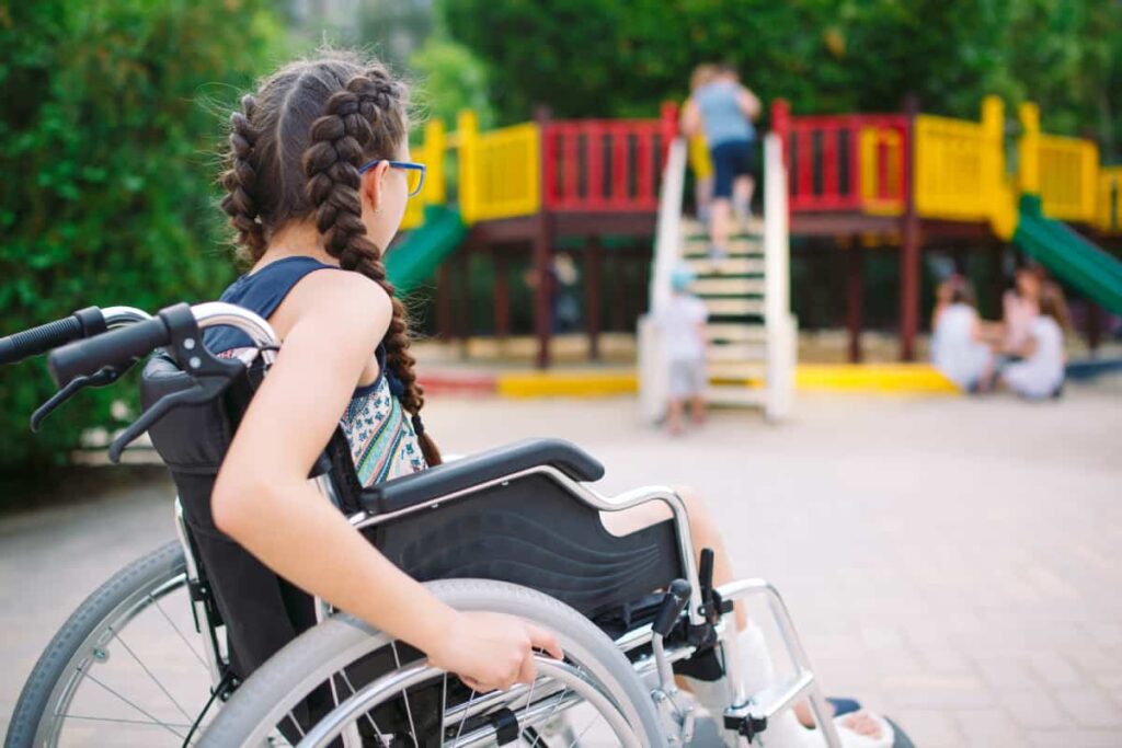 Girl in a wheelchair watching kids playing at the playground