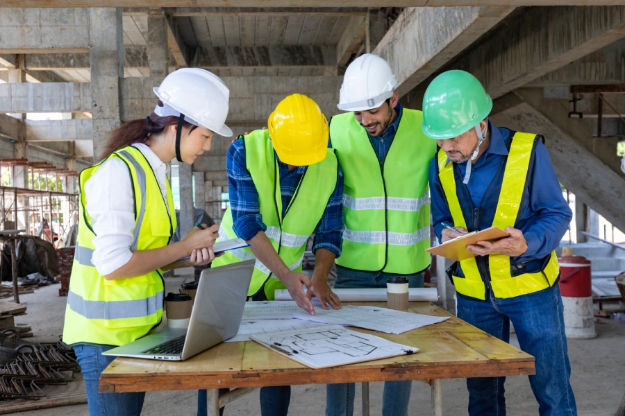 Diverse team of specialists use tablet computer on commercial construction site.