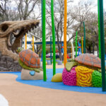 Playground structures in the shape of turtles and a dinosaur skeleton adorn a modern playground.