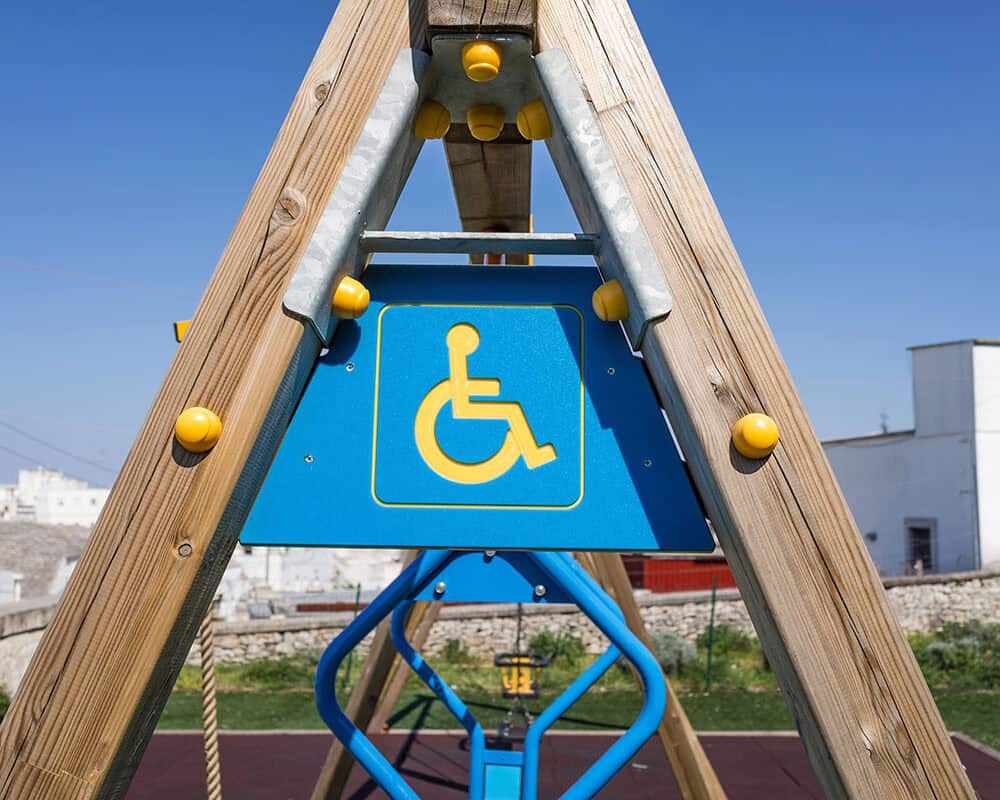 A wooden playground structure featuring a blue sign with a yellow wheelchair symbol, indicating accessibility for individuals with disabilities, against a clear blue sky.